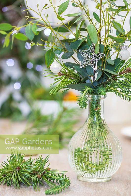 Table decoration featuring a glass vase filled with foliage decorated with silver stars and mini baubles