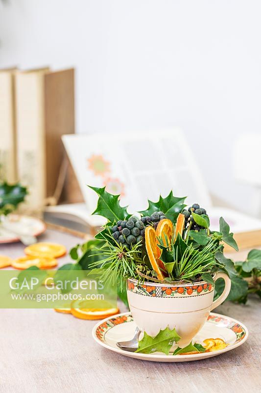 Table decorations including teacup filled with Holly, Ivy berries, Pine foliage and dried orange slices