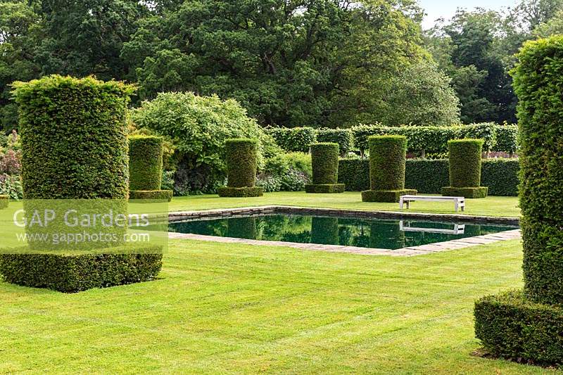 Clipped Yew columns - Taxus baccata - and reflective pool in the Silent Garden at Scampston Hall Walled Garden, North Yorkshire, UK. 