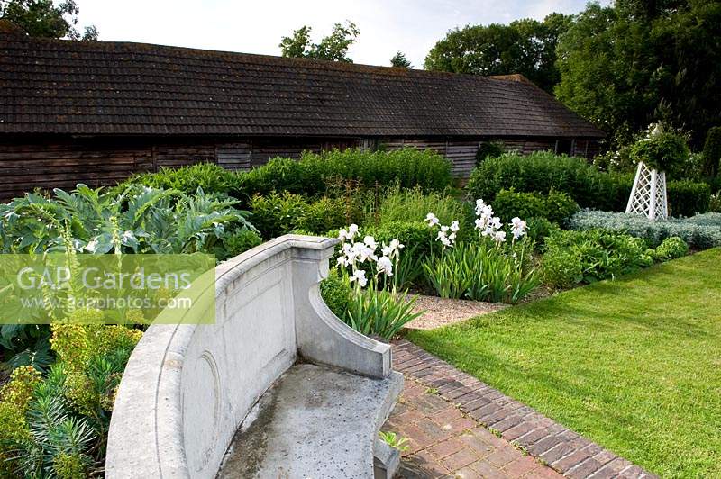Curved stone seat in country garden with large barn. 