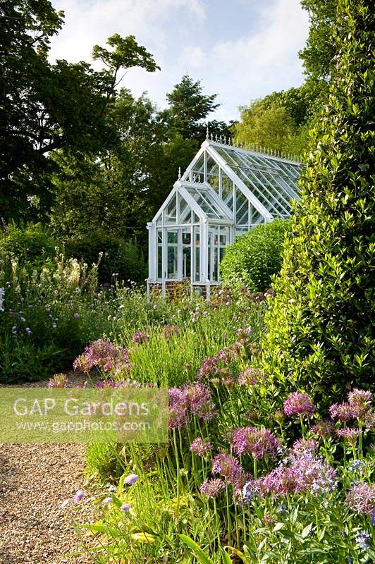 White Victorian style glasshouse in cottage garden. 