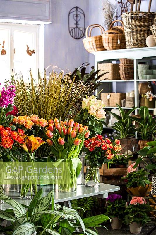 View of flower shop interior, with glass vases of flowers and baskets displayed on shelves. 