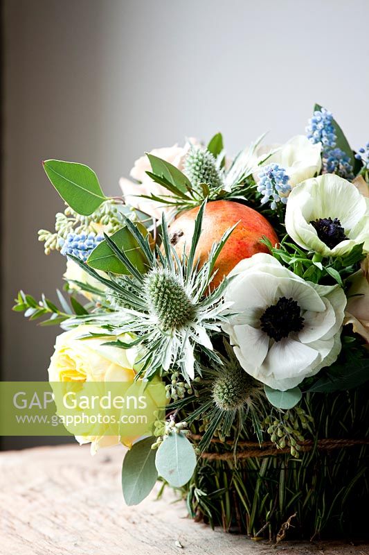 Floral basket display filled with rose 'catalina', dianthus 'antique', eryngium, muscari, pomegranates and white anemones