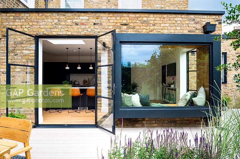 Modern extension to a brick house with doors opening out onto deck and large window with seat