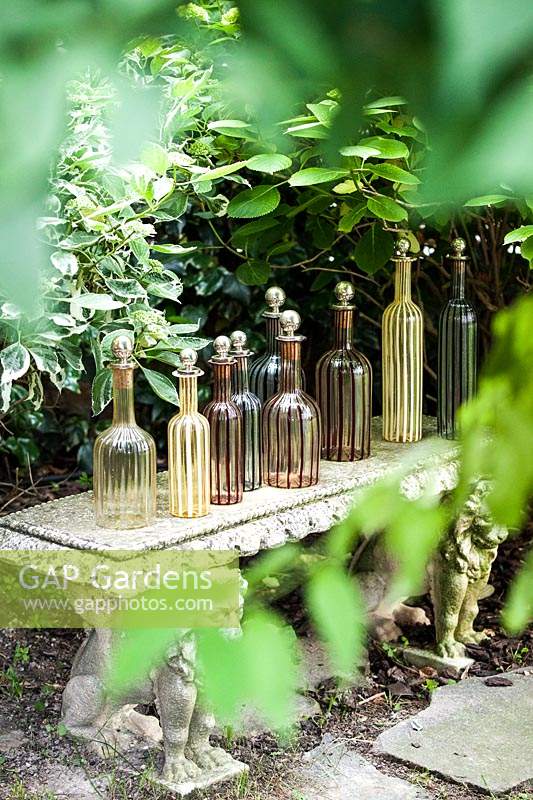 Murano glass vintage bottles displayed in stone bench in garden. 