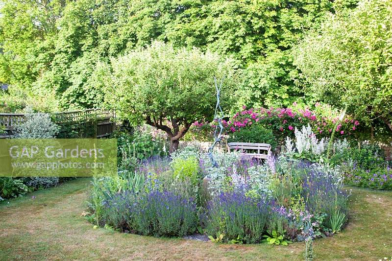 Summer garden with central sculpture in bed of Lavender, Salvia turkestanica, Eryngium, Dianthus, and Rosa 'American Pillar' 