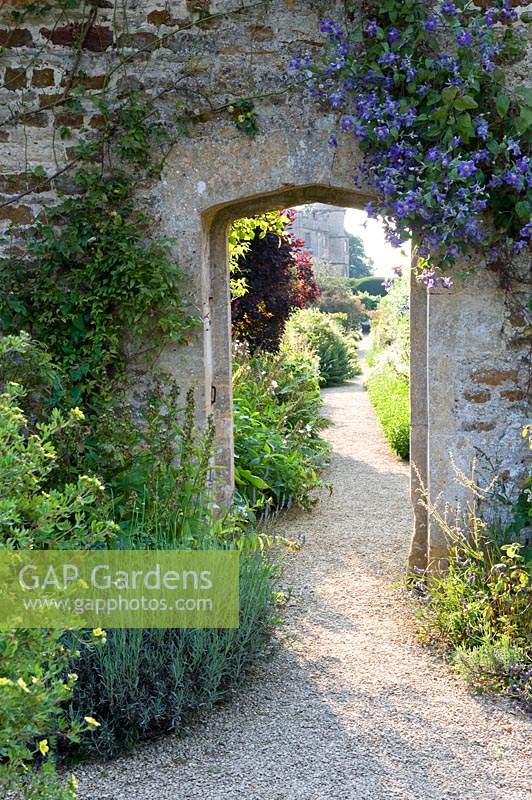 Stone arch in wall through to separate garden along a gravel path