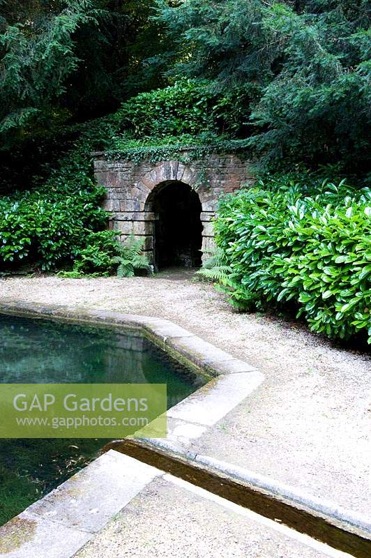 Water feature pond fed by rill, gravel path and stone tunnel arch through earthwork