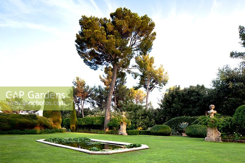 Formal pond set in a lawn, topiary and trees beyond