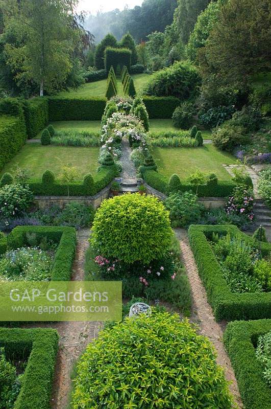 Overview of formal garden with parterre, brick path Prunus lusitanica - Laurel - and a Rosa - Rose - arch