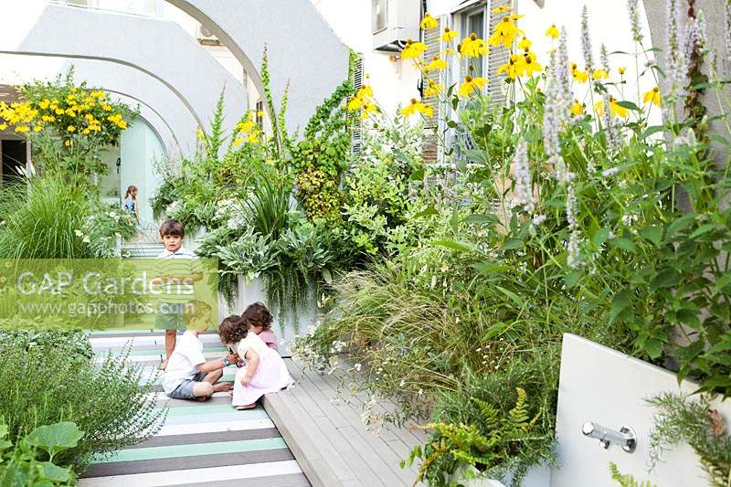 children play on the terrace with container grown perennial grasses and herbaceous plants