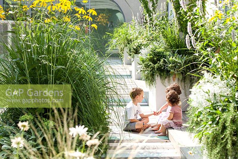 Children play on the terrace with container grown perennial grasses and herbaceous plants