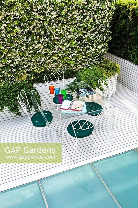 Table and chairs in modern terrace garden surrounded by evergreen planting.