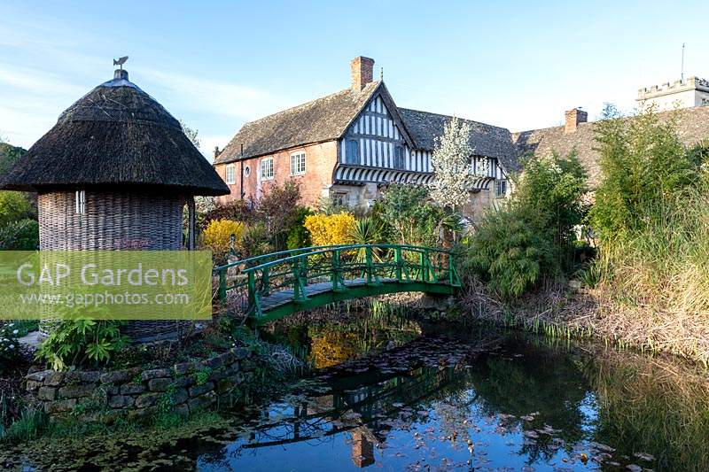 A Monet bridge crosses a pond and leads to a summerhouse with thatched roof