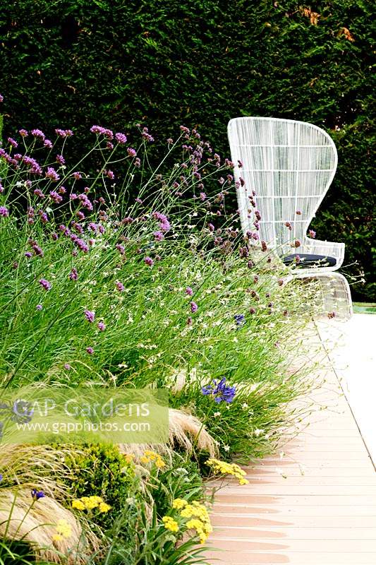View along perennial border to modern, white chair in garden. 