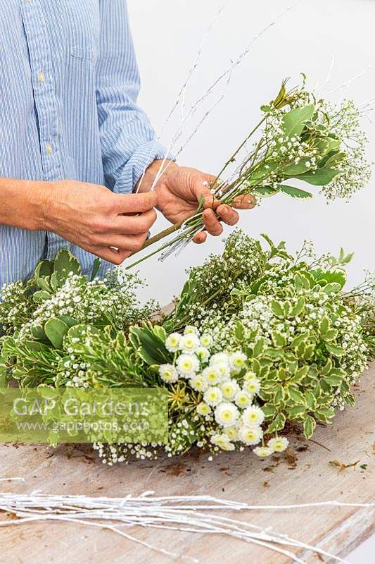 Woman adding white painted twigs to wreath bundle. 
