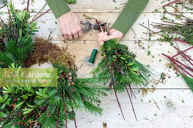 Woman using secateurs to trim stems of a bundle of winter foliage and cuttings