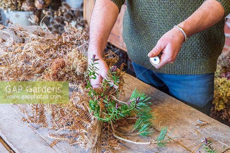 Man using floristry wire to attach hebe stems to wreath