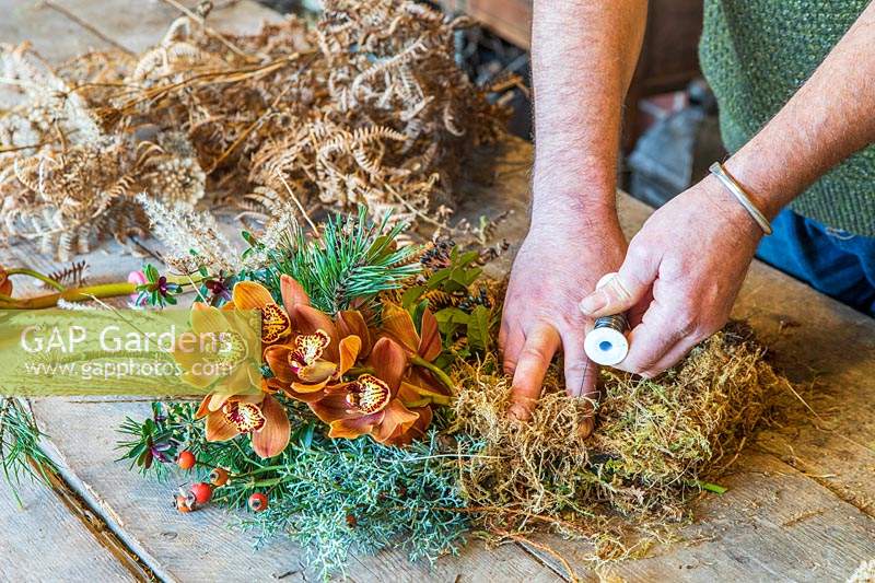 Man using floristry wire to attach moss to wreath form