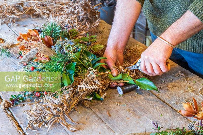 Man using garden sissors to trim excess off a wreath