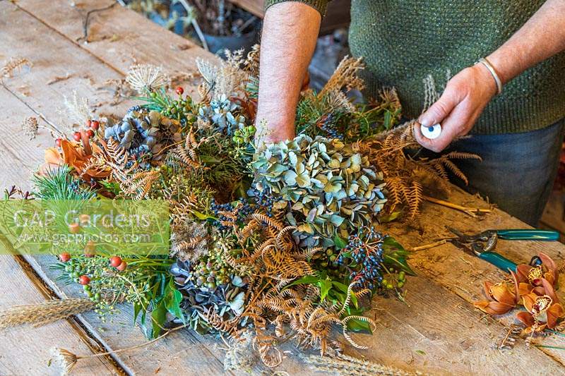 Man using floristry wire to attach flower heads to wreath
