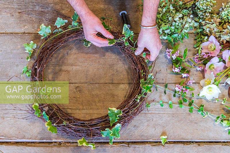 Man arranging ivy onto rustic birch wreath form. 