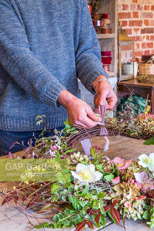 Man attaching pink ribbon to a rustic wreath
