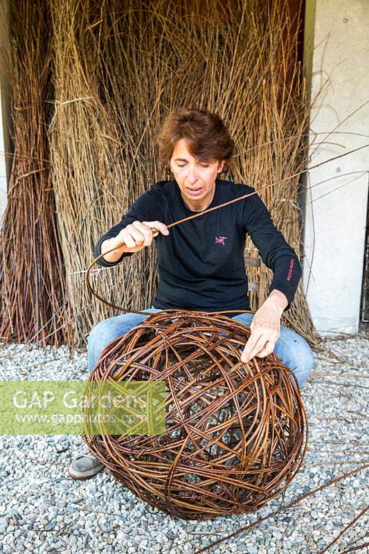 Woman making ornamental sphere out of woven willow stems.