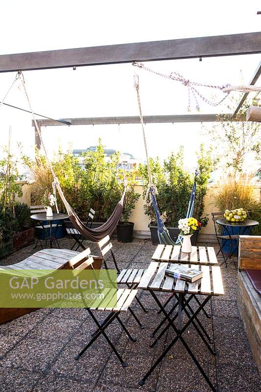 Seating area and hammocks are surrounded by potted plants on roof garden of hostel.