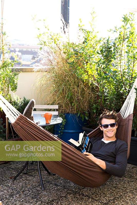 Guest relaxes in hammock on the hostel's terrace, surrounded by Mediterranean plants. 