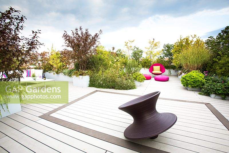 Terrace with decking and in the foreground Spun chair by Magis design, in the background a bright pink chair and cushions surrounded by shrubs 