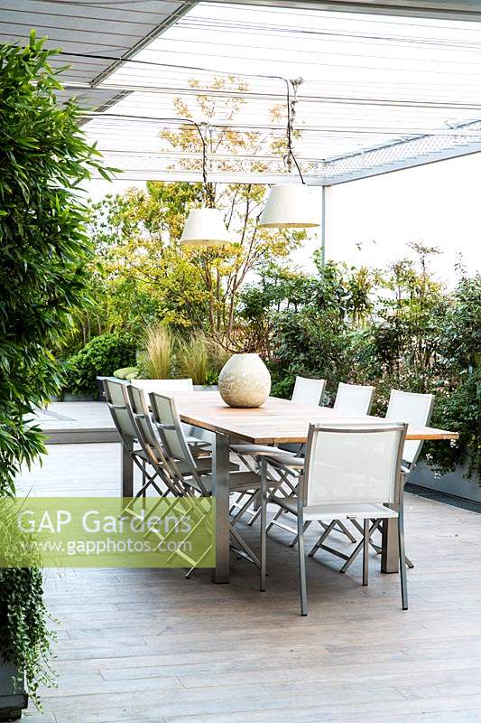 Covered dining area on terrace screened by container grown shrubs 