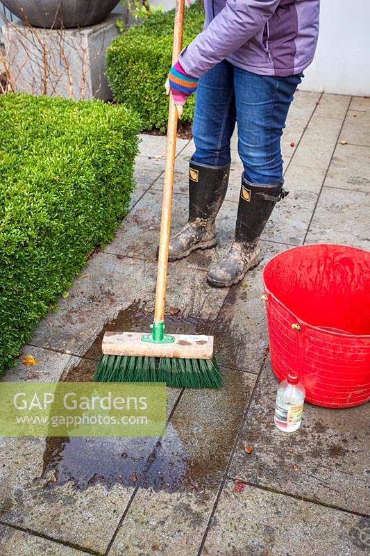 Cleaning a patio using a long-handled brush, water and vinegar