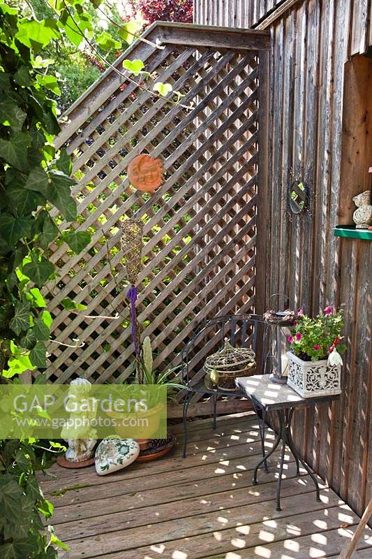 Trellis panel attached to fence and small deck, provides a corner to display a collection of ornaments and container plants 