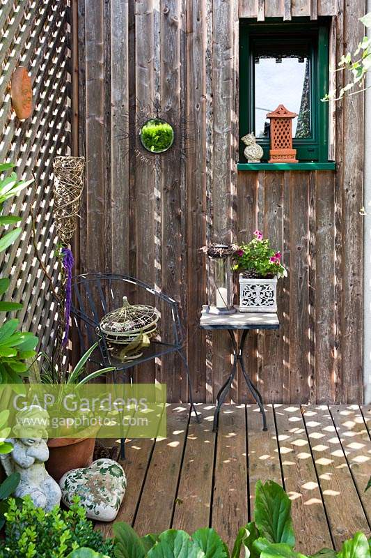 Small decked patio with a display of ornaments including mirror, statue and pot plants