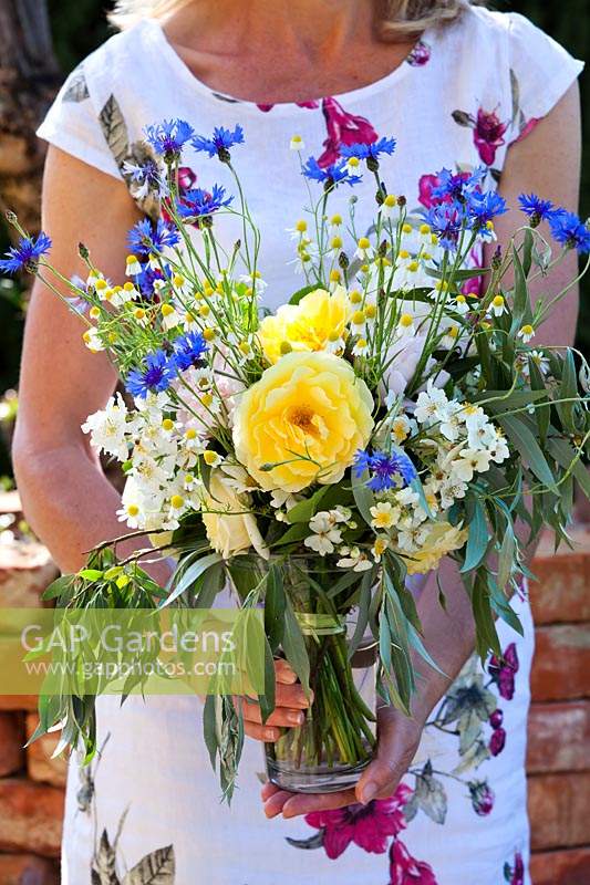 Woman with bouquet of early-summer flowers, including yellow roses. cornflowers and chamomile.