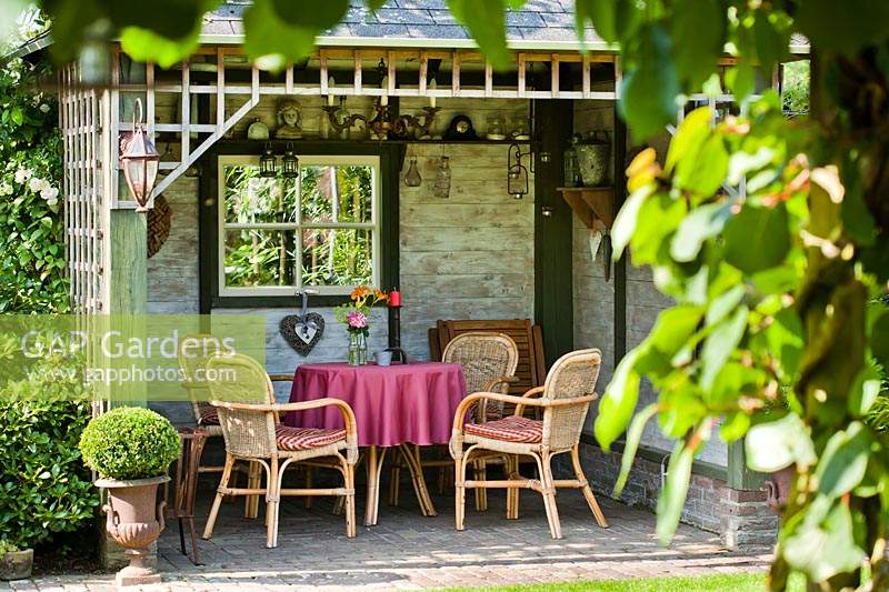 Outdoor relaxing area, table and chairs inside open-fronted summerhouse with window and trellis top 