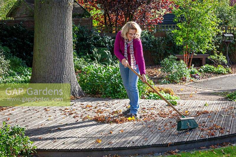 Sweeping fallen leaves off wooden decking with a brush in early autumn to prevent it getting slippy