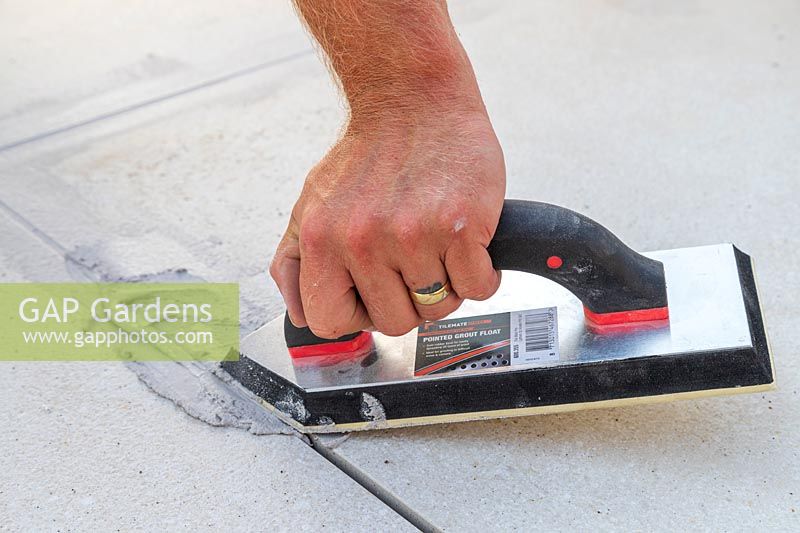 Man using a grout float to fill context Porcelain patio with porcelain grout