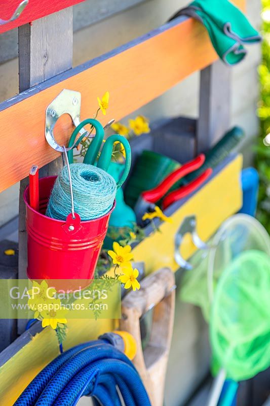 Close up detail of rainbow coloured pallet organiser holding various garden tools