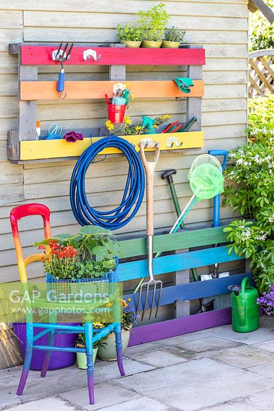 Rainbow coloured pallet tool organiser attached to outside wall of a shed with matching chair 