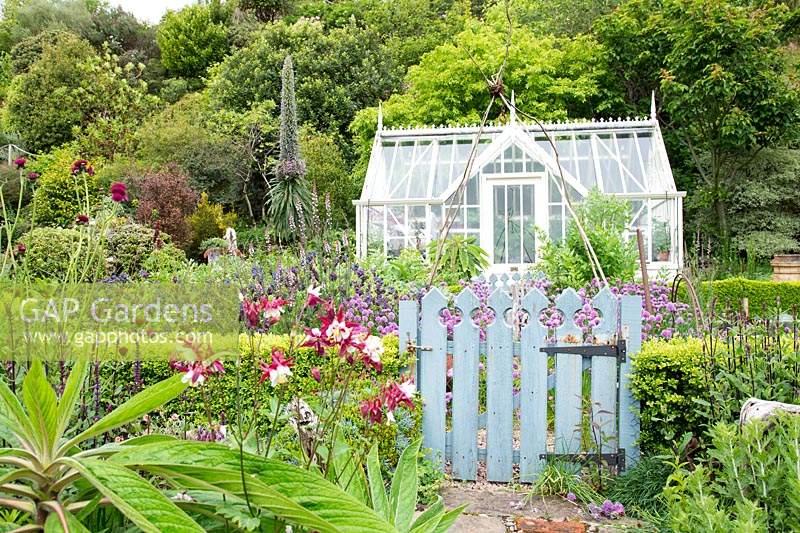 View of gate into kitchen garden with traditional greenhouse, beyond hills with trees  