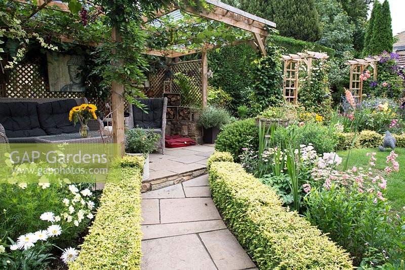 Path leading to a dining area under wooden pergola in cottage garden 