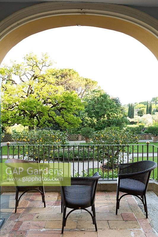 View from inside the house from balcony with seating, out to parterre garden and a Diospyros kaki - Persimmon Tree