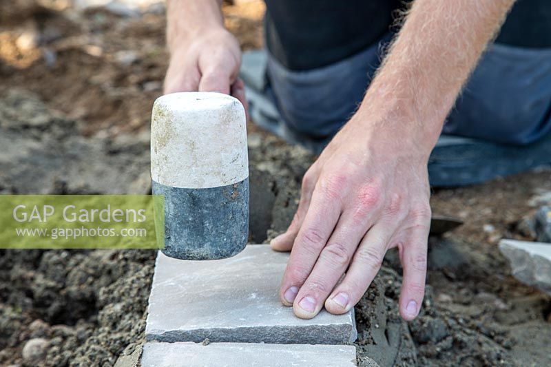 Man using rubber mallet to level freshly laid sandstone setts