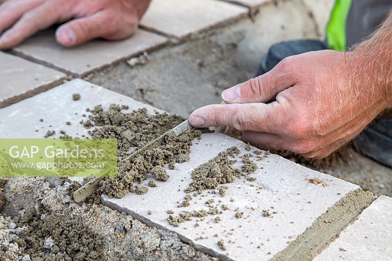 Man using pointing trowel to fill paving joints with pointing material