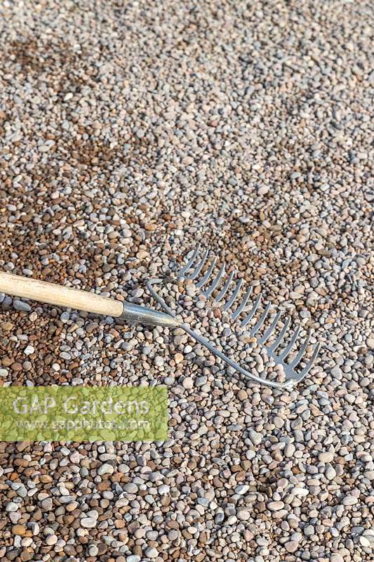 Using the back of a rake to spread 'scottish pebbles' gravel on path
