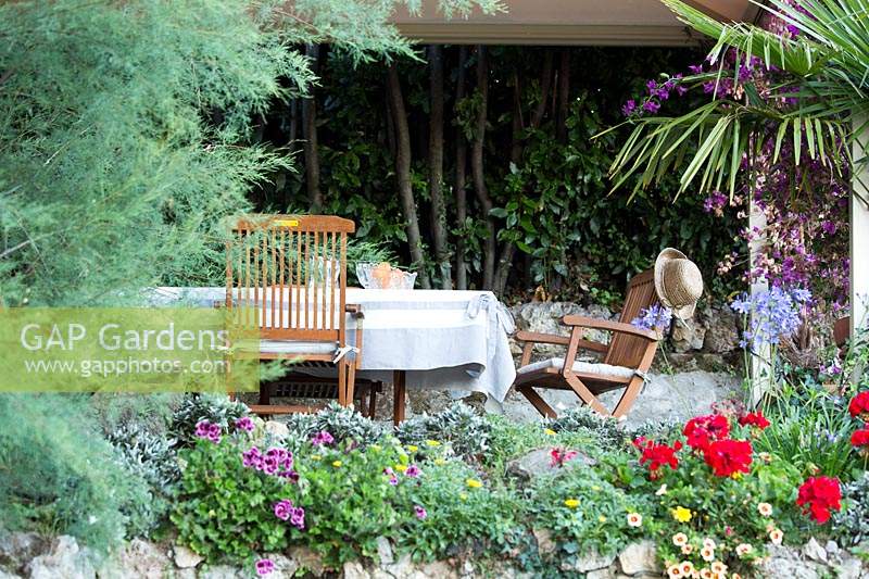 View over stone wall with colourful bedding flowers to a shaded dining area 