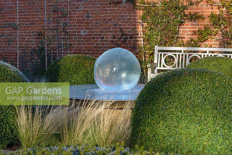 Aqualens water feature designed by Allison Armour with large clipped balls of Buxus sempervirens and Stipa tenuissima grass 