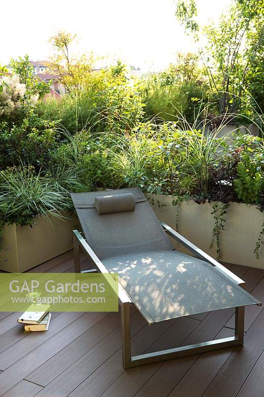 Sun lounger on decked terrace with a living screen of shrub and perennial foliage in trough planters 